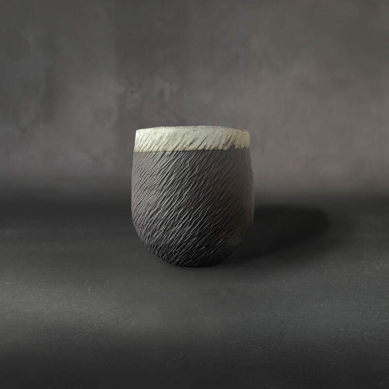 Hand-built, carved black midfire cup with white dolomite glaze